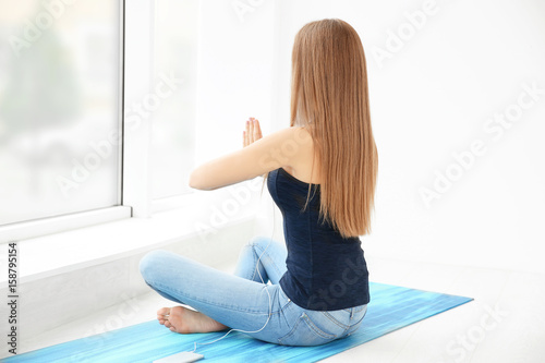 Young woman practicing yoga and listen to music near big window