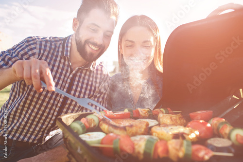 Friends making barbecue and having lunch in the nature. Couple having fun while eating and drinking at a pic-nic - Happy people at bbq party