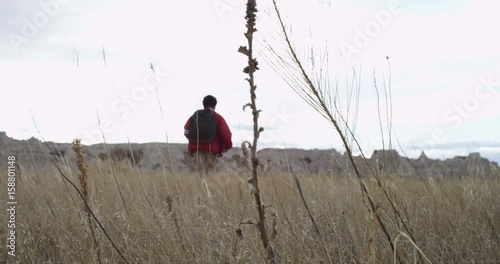 Low angle, young boy with backpack runs in field, slow motion