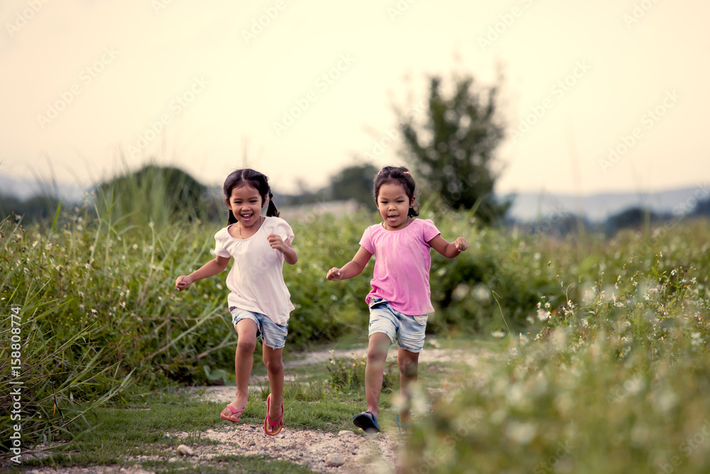 Two asian little girls having fun and running together in the park in vintage color tone Two asian little girls having fun and running together in the park in vintage color tone
