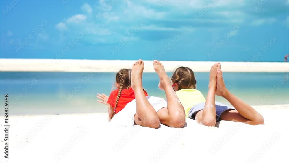 Little girls having fun at tropical beach lying together on the seashore. SLOW MOTION