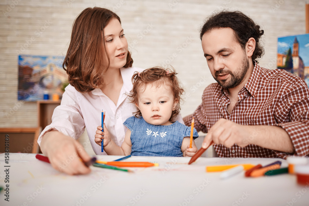 Portrait of young family with little cute girl drawing together in art class using crayons Portrait of young family with little cute girl drawing together in art class using crayons