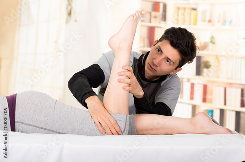 Massage and rehabilitation. Handsome massage therapist massaging a patients calf, in a doctor office background