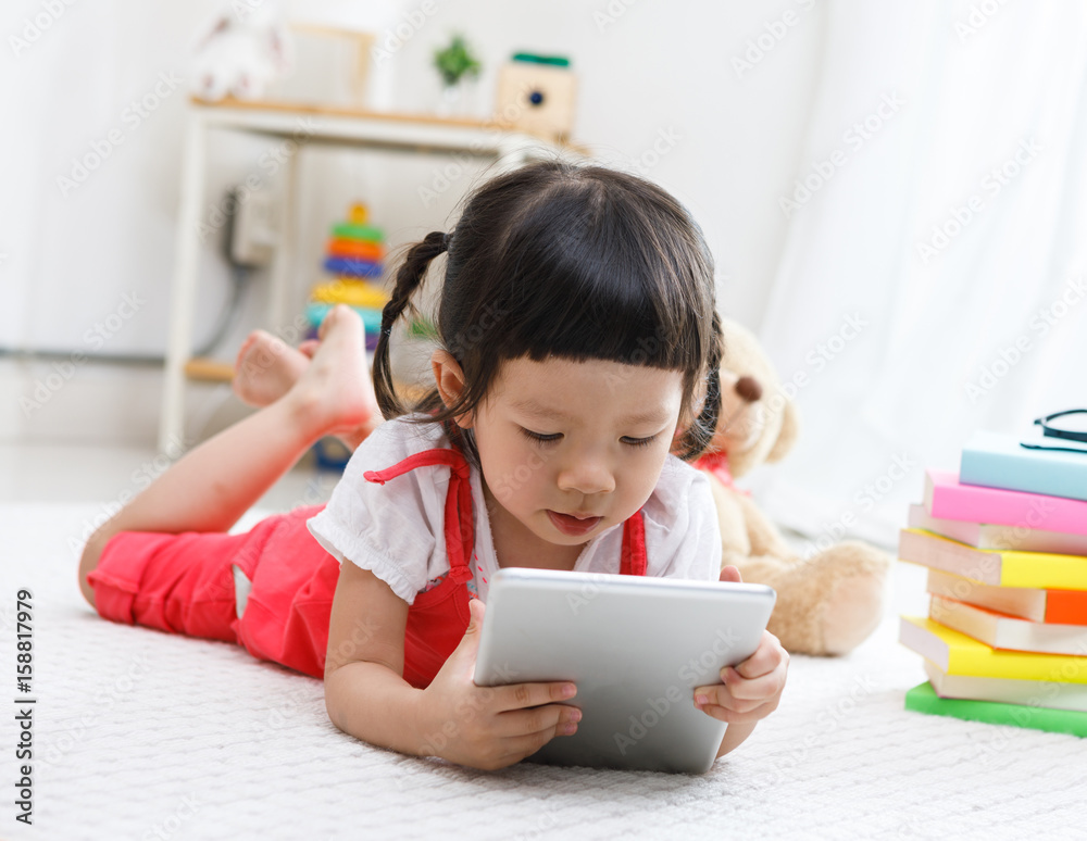 Preschooler girl plaing tablet. Cute child reading with teddy bear. Little girl having fun indoors at home, kindergarten or Preschooler girl plaing tablet. Cute child reading with teddy bear. Little girl having fun indoors at home, kindergarten or