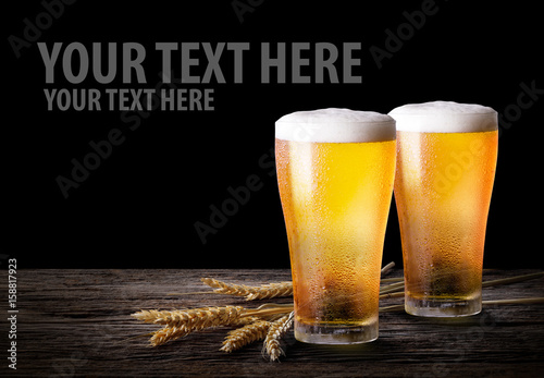 Cold beer with wheat on wooden table. Glasses of light beer on the isolate black  background with copy space.
