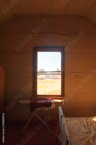 Abandoned room in Australian ghost town with iron board in old house, view through window with dry outback landscape in background.