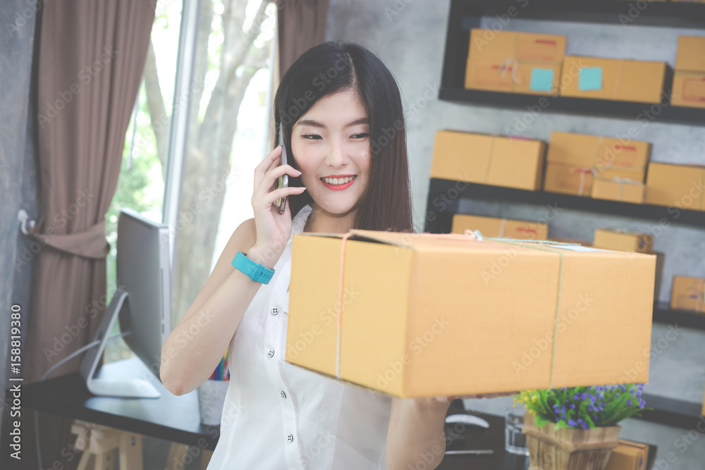 Asian woman entrepreneur is using phone and showing the box packing at home workplace. Asian woman entrepreneur is using phone and showing the box packing at home workplace.