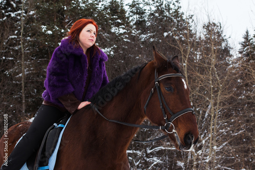 Woman with red hair and big horse outdoor in winter