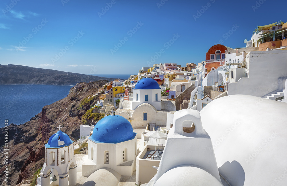 Fototapeta premium Santorini blue dome churches on the steep cliff, Greece. Cyclades Islands.