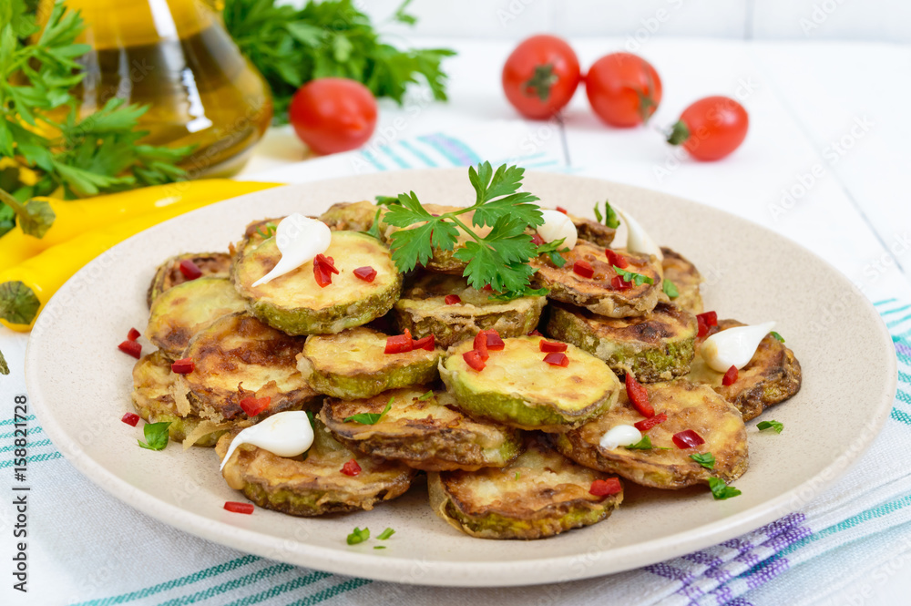 Spicy salad of fried slices of zucchini and young garlic, spices, herbs and red pepper on a plate on a white wooden background. Spicy salad of fried slices of zucchini and young garlic, spices, herbs and red pepper on a plate on a white wooden background.