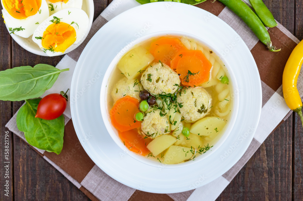 Light dietary soup with meat balls, vegetables, fusilli and boiled eggs on a dark wooden table. Useful lunch. The top view Light dietary soup with meat balls, vegetables, fusilli and boiled eggs on a dark wooden table. Useful lunch. The top view