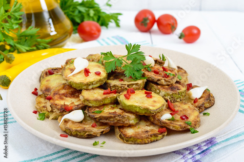 Spicy salad of fried slices of zucchini and young garlic, spices, herbs and red pepper on a plate on a white wooden background.