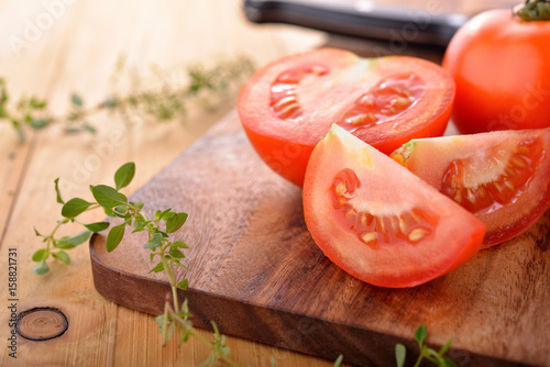 whole and portion cut fresh tomato with herb on cutting board