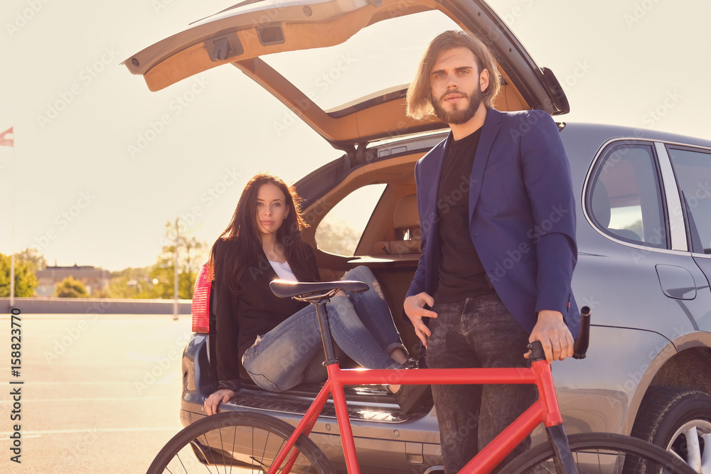Obraz premium Couple with single speed bicycle near the car with open trunk.