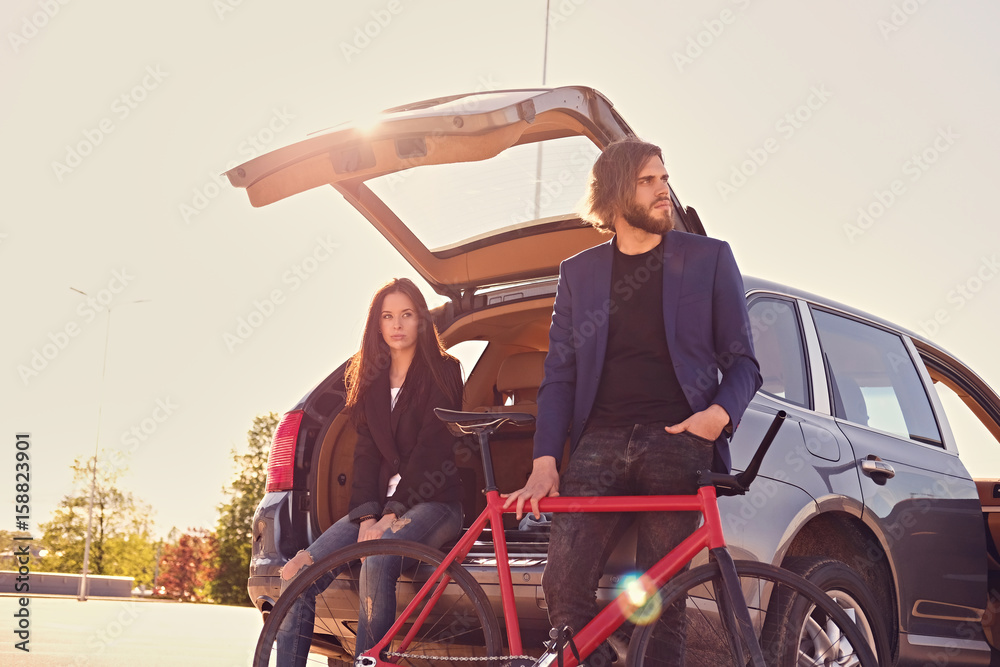 Obraz premium Couple with single speed bicycle near the car with open trunk.