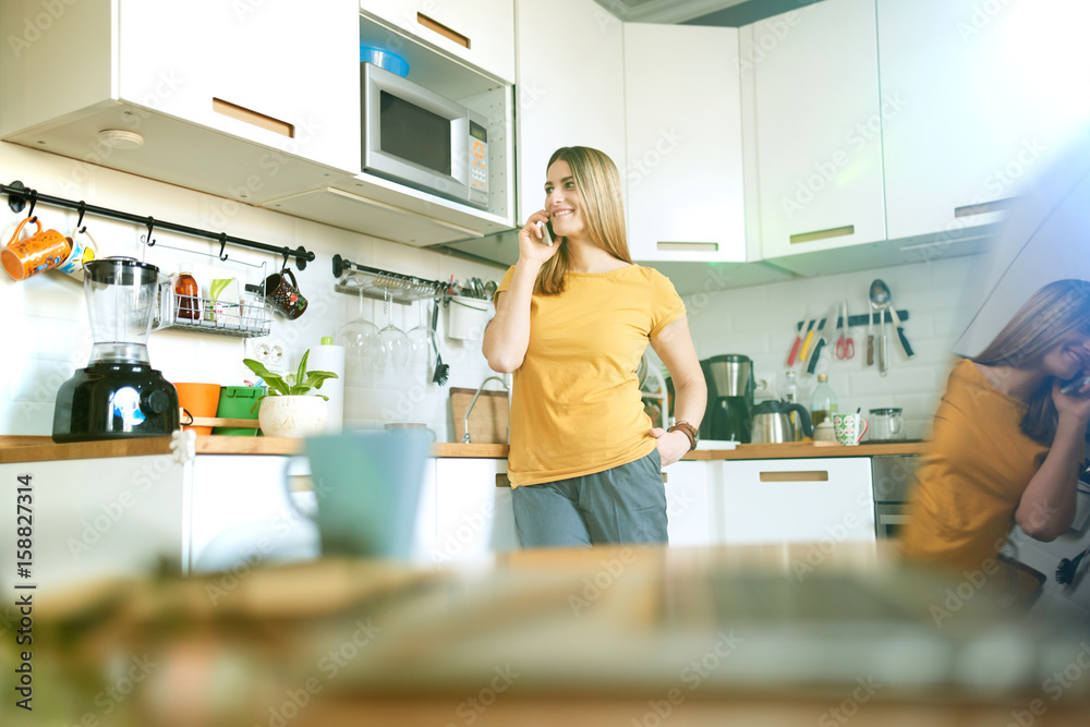 Young woman standing in a kitchen with mobile phone Young woman standing in a kitchen with mobile phone