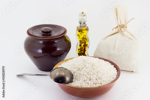 The composition of Rice groats in a clay pial next to a clay pot and a copper spoon, photo