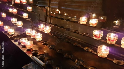 Numerous Christian Catholic votive candles being lit in some cathedral installed on some metal racks. They glimmer and remind about some eternal things, including the impermanence of our life