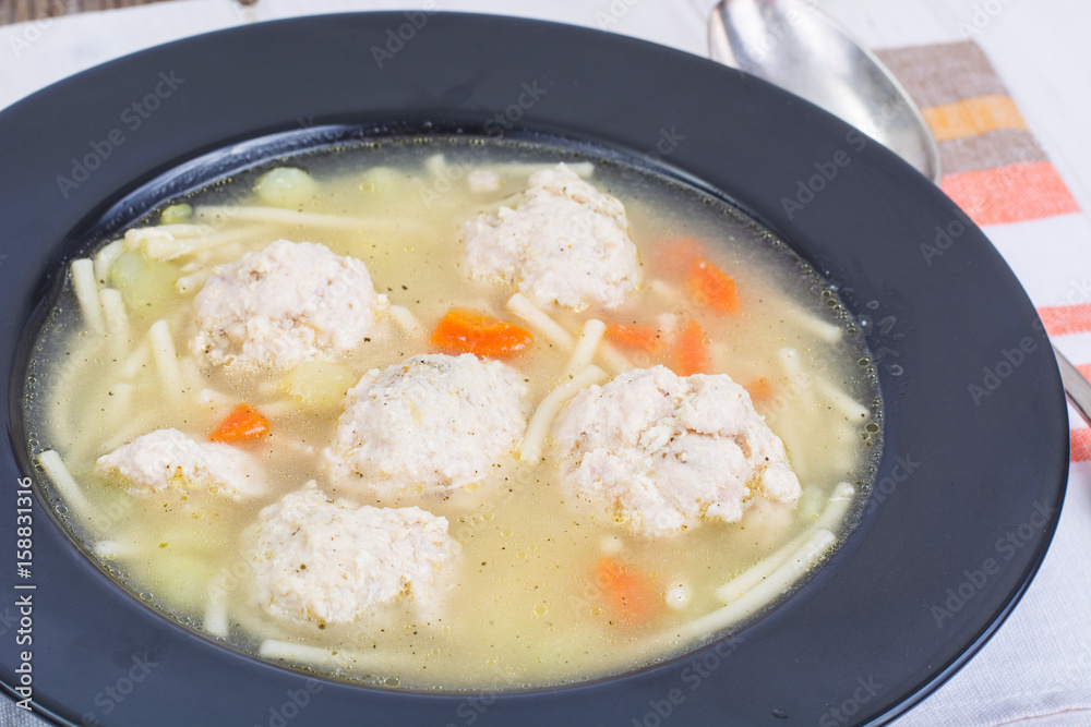 Soup with noodles and meatballs in ablack plate Soup with noodles and meatballs in ablack plate