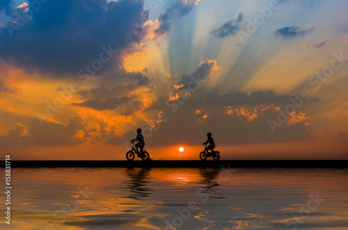 Silhouette,Two children cycling on a sunset bike and shining on the beautiful water.