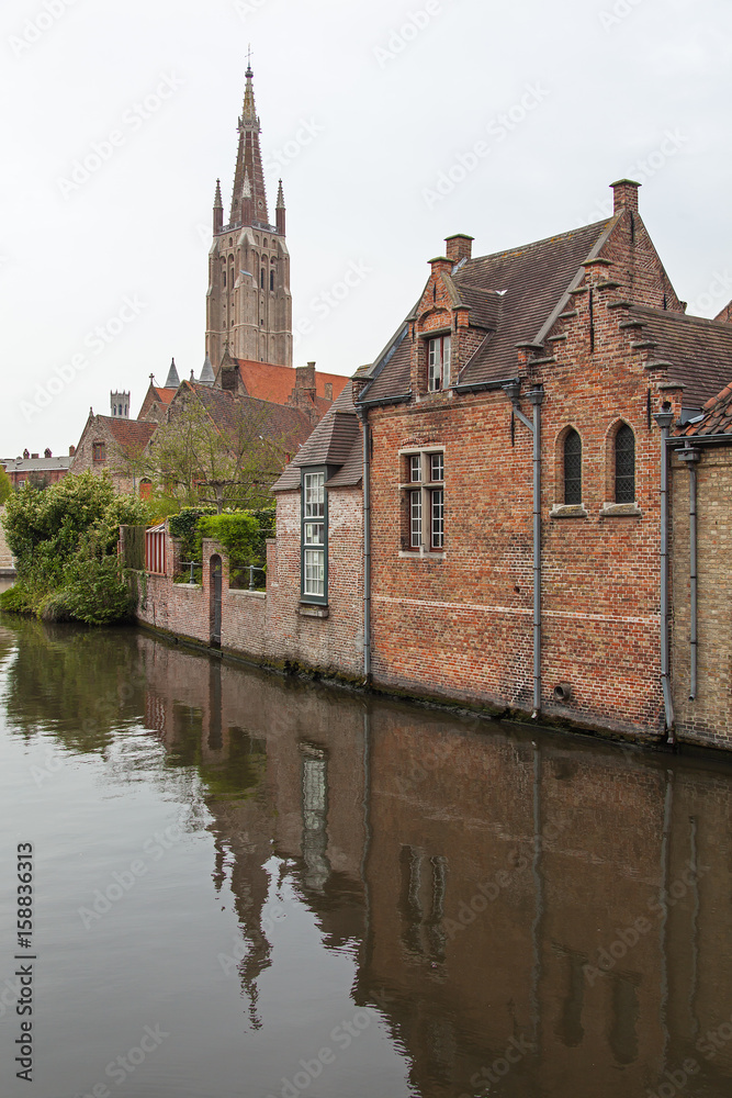 Scenic old red brickwork buildings on the canal  with Church Our Lady tower in the background in medieval neighborhood of Bruges (Brugge), Belgium