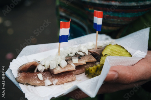 Konstfotografi A hand holds a traditional Dutch delicacy of herring with gherkins and onions