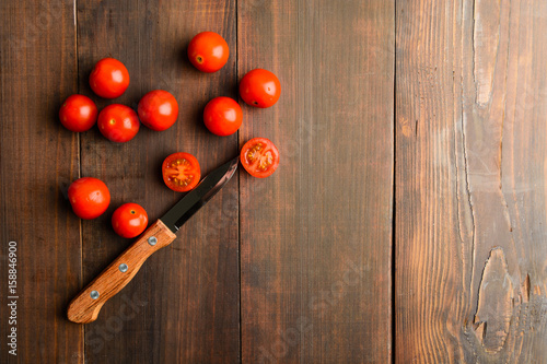Cherry tomatoes with one of them cuuting over brown wooden table