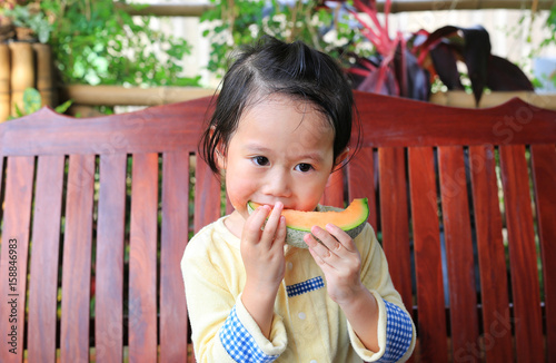 Child girl eating sliced cantaloupe melon.