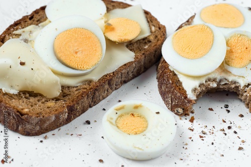 Two bread with sliced boiled egg, second is bite taken.