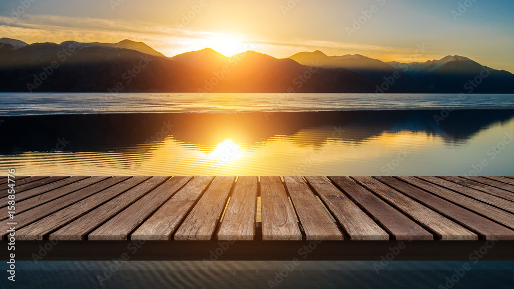 Wooden bridge on the lake with a reflection of sunset on the snow mountain