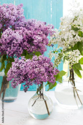 Three bouquets of lilac in round transparent vases near window