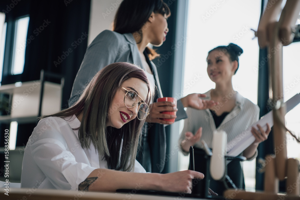 Obraz premium Young businesswoman in eyeglasses using graphic tablet while colleagues standing behind
