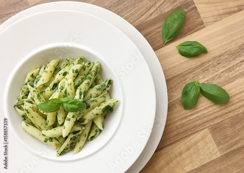 Penne pasta with spinach pesto. Basil leaves on side. Top view.