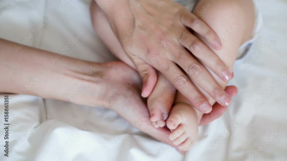 mother touching feet of a newborn baby lying in white bed mother touching feet of a newborn baby lying in white bed