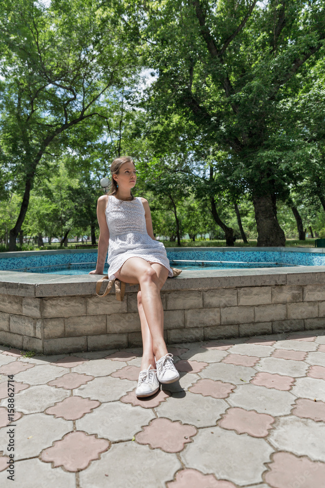 Young beautiful girl in short white dress sit near fountain Young beautiful girl in short white dress sit near fountain