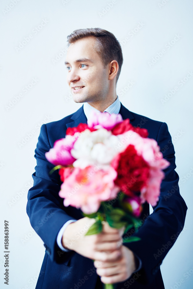 Portrait of young man in suit posing with bouquet of beautiful flowers standing against white wall Portrait of young man in suit posing with bouquet of beautiful flowers standing against white wall