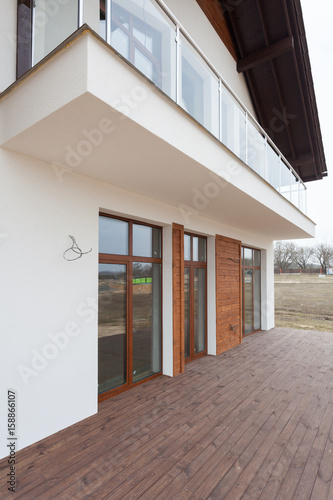 New house with white walls  wooden terrace and .glass balcon