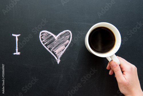 Top view of I love heart doodle drawing on chalkboard with human hand holding cup of coffee