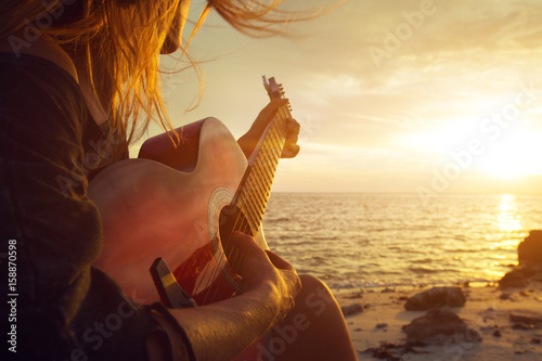 Beautiful young woman playing guitar on sunset beach