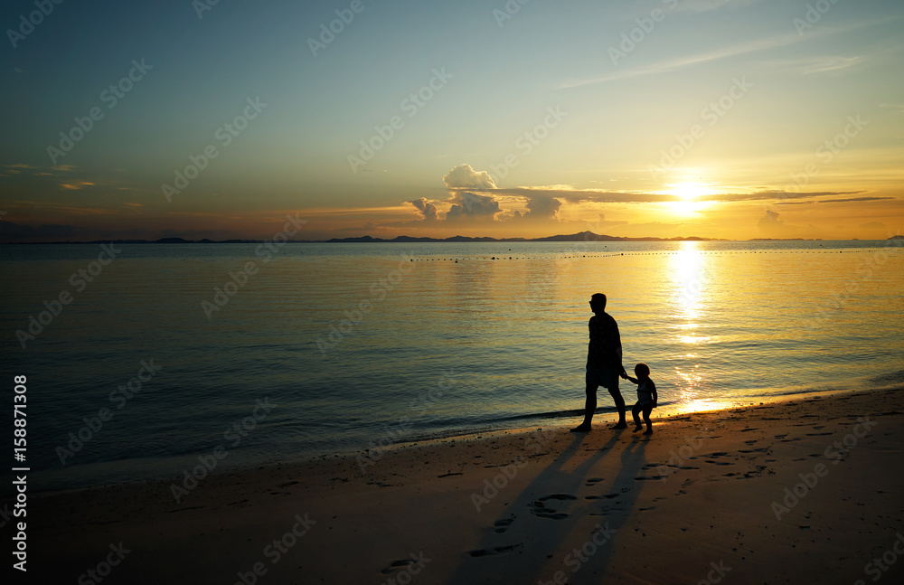 Father and his child walking on sunset beach , silhouette shot .