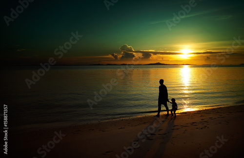 Father and his child walking on sunset beach , silhouette shot and tone image .