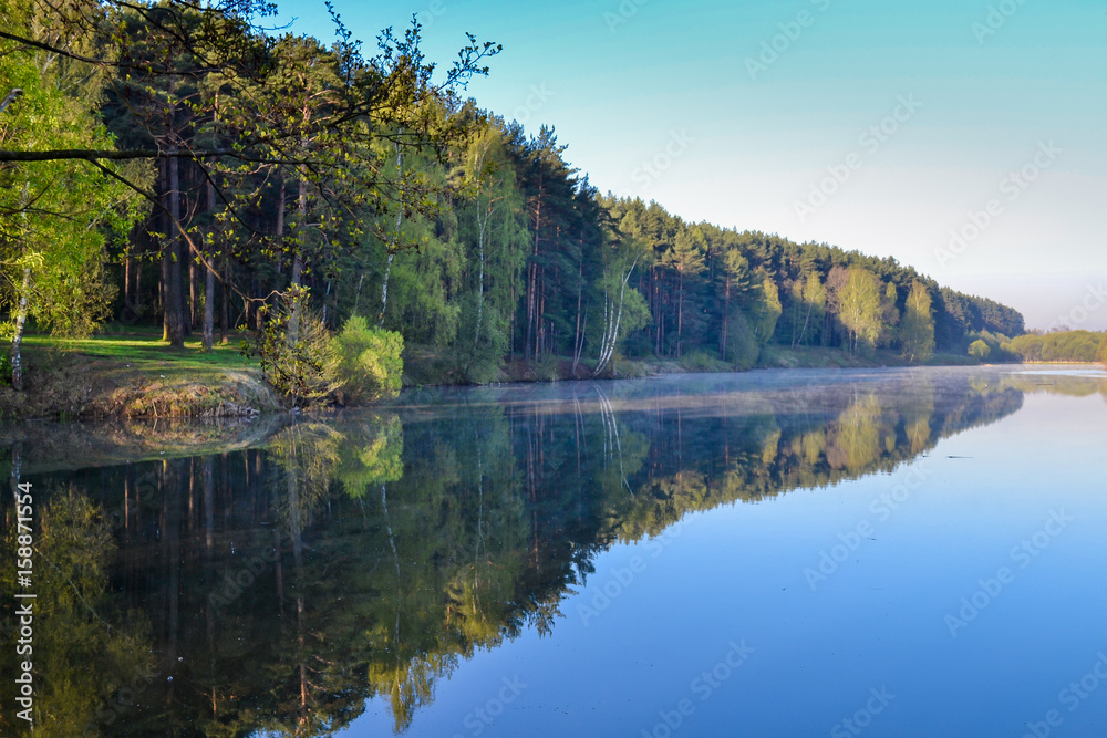 Forest and sky reflected in the calm blue water of Lake Forest. Early morning. Relax and silence