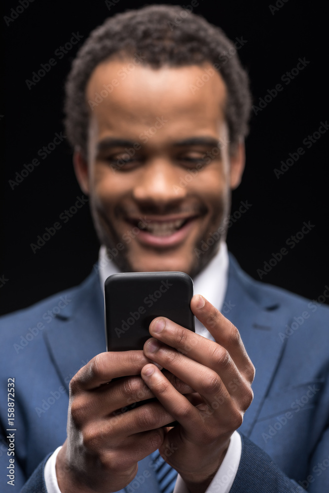 Portrait of afro american businessman messaging on smartphone isolated on black