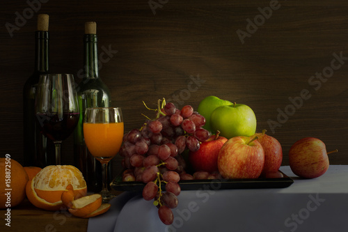 Pile of Fruits and bottle wine with glass put on the plank in dim light / Still Life image and selective focus .