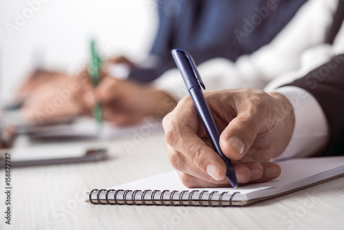 Cropped shot of businessman holding pen and writing in notebook while sitting at table