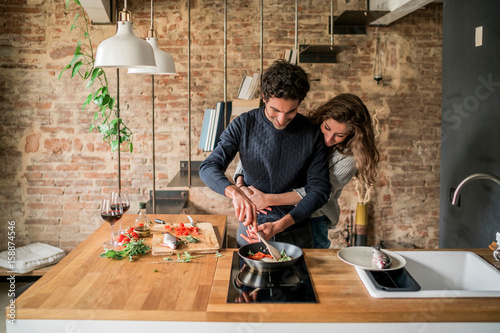 Young couple cooking fish cuisine at kitchen counter hob photo