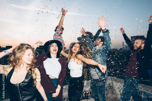 Group of friends dancing, enjoying roof party, confetti in air photo
