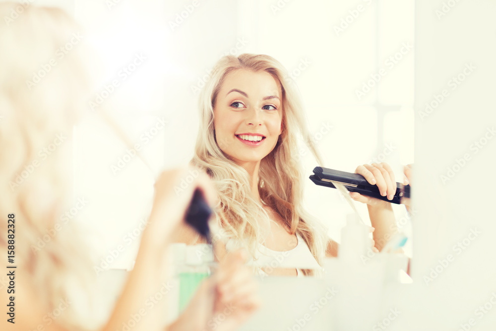 Fototapeta premium woman with styling iron doing her hair at bathroom