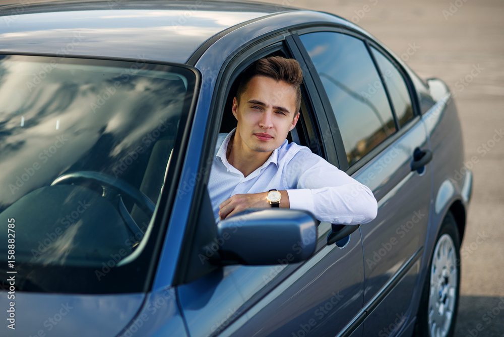 Attractive handsome successful man in white shirt driving an expensive car