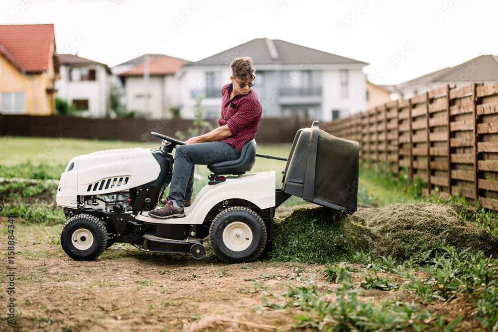 Gardner trimming and unloading cut grass from the garden using a ride on lawn mower
